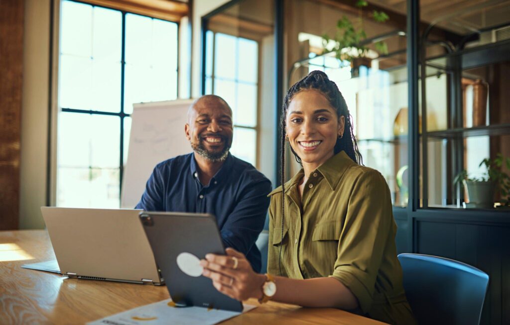 Cheerful female executive and colleague smiling at camera in boardroom