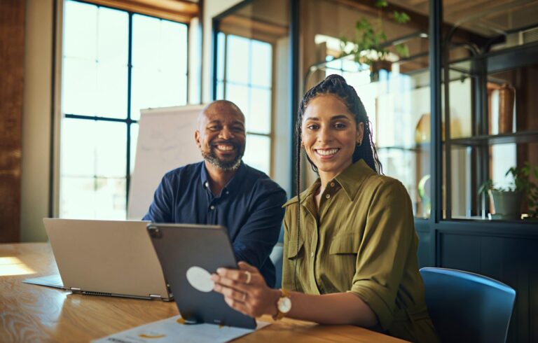 Cheerful female executive and colleague smiling at camera in boardroom